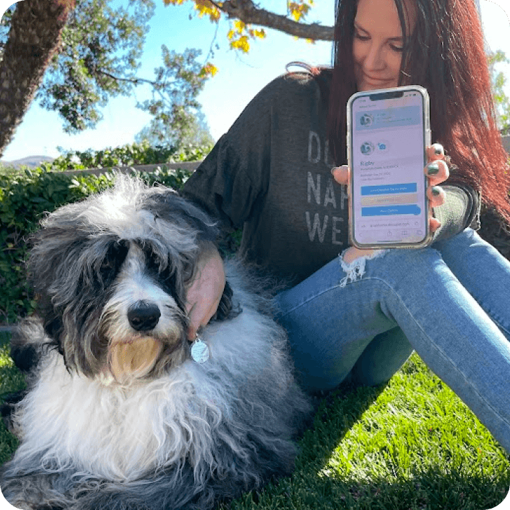 A woman holds her phone out, showing her dog's online pet profile while holding her dog's pet tag.