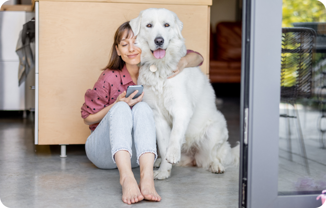 A woman hugs her dog while looking at her phone.