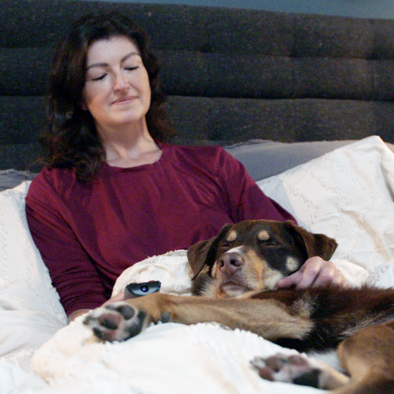 A woman sits in bed with her sleeping dog.